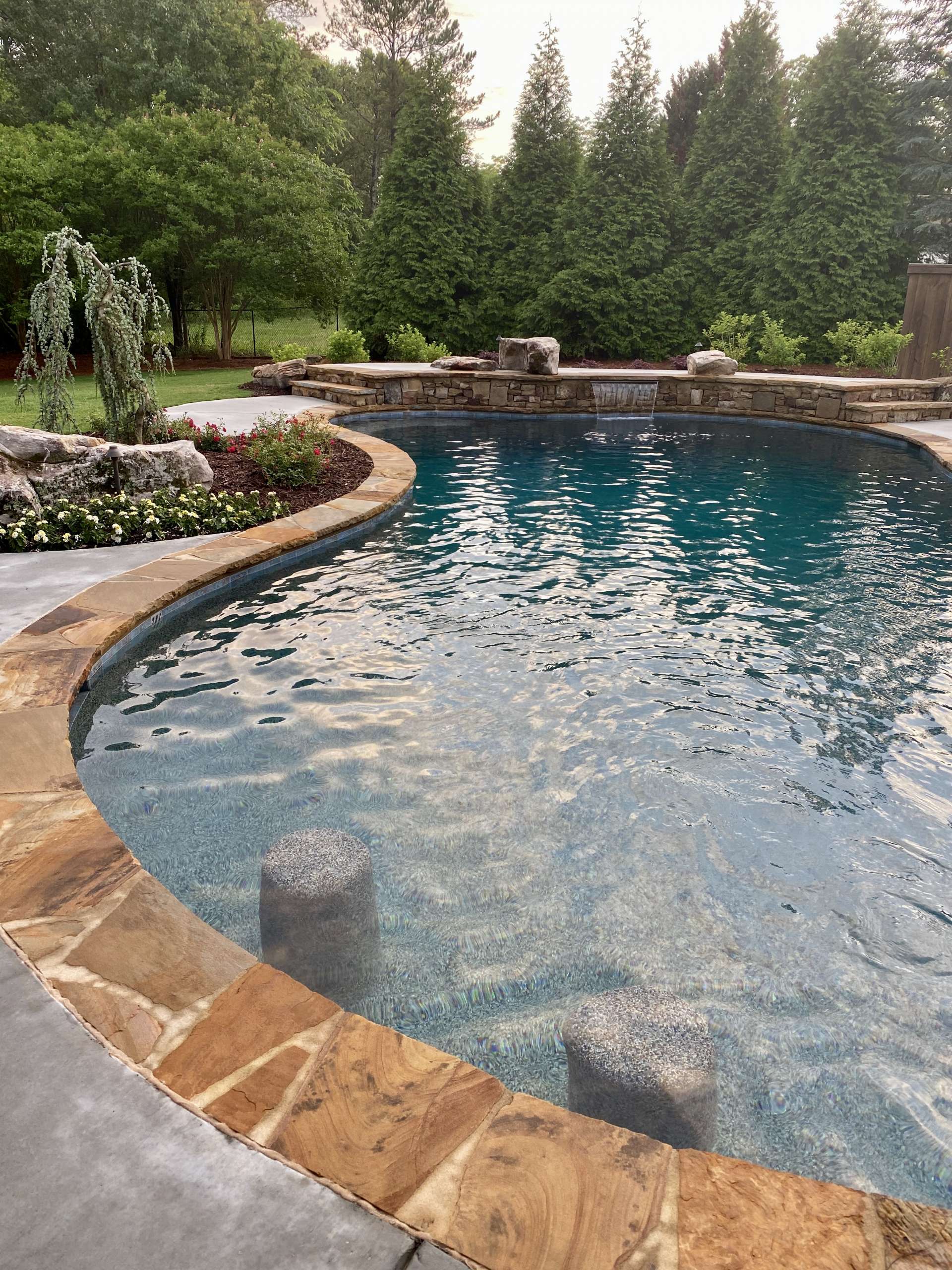 Close up photo of turquoise pool with stone edge and waterfall